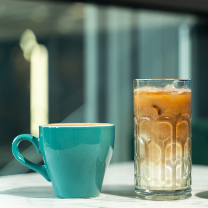 A turquoise cup next to a tall glass of iced coffee on a table in london coffee shop