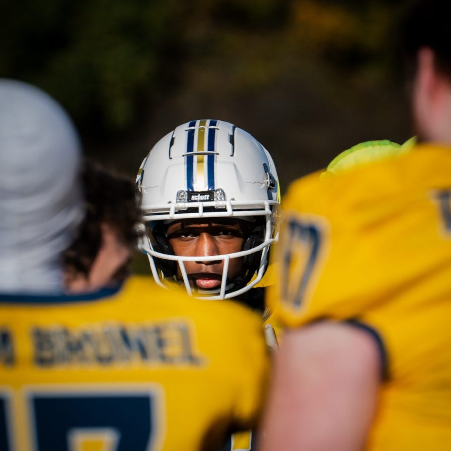 A focused american footballer player in a helmet surrounded by teammates in yellow jerseys at london field