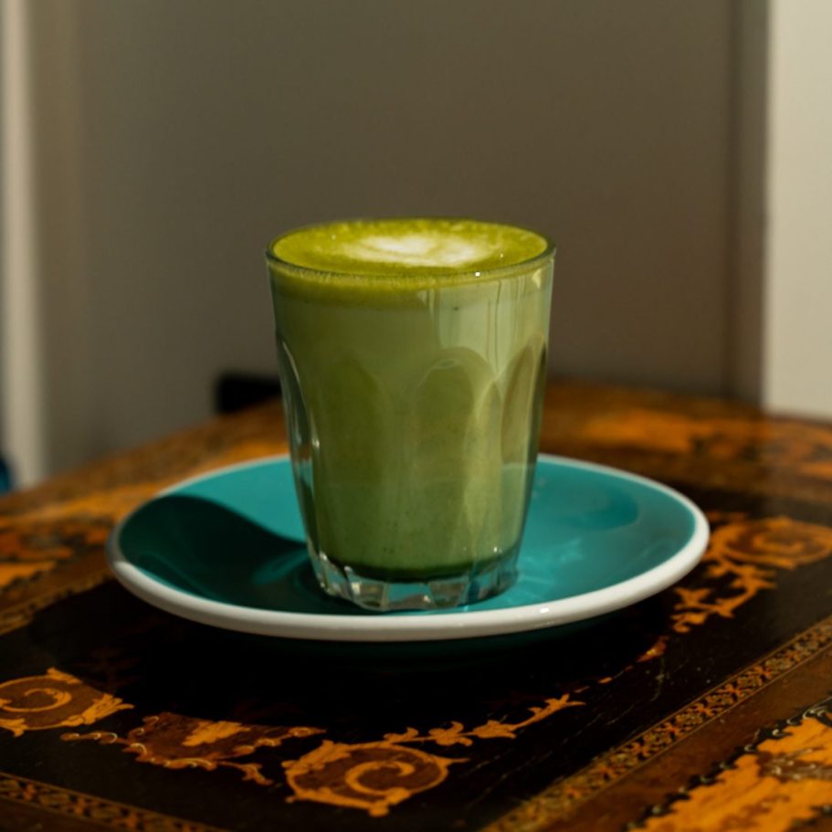 A glass of green matcha tea on a turquoise plate resting on a wooden table in london 