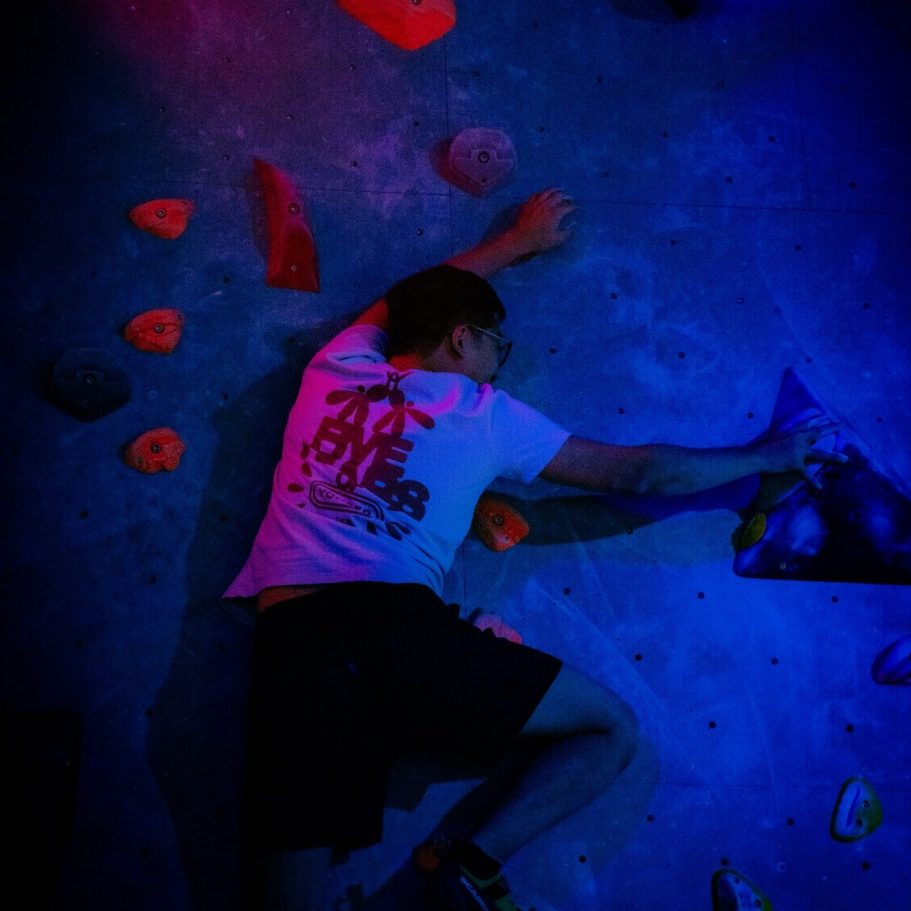 A climber at a uv party at indoor bouldering wall in london reaching for holds.