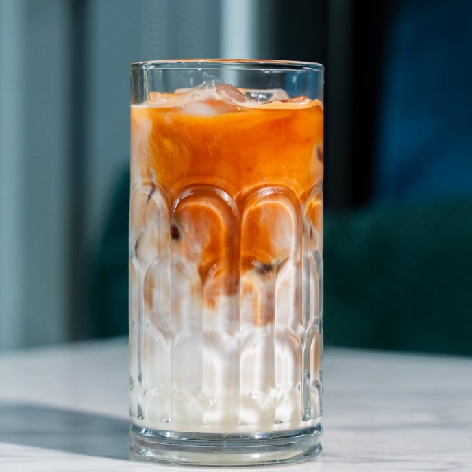 Tall glass of iced coffee with vibrant orange crema on top in london coffee shop 