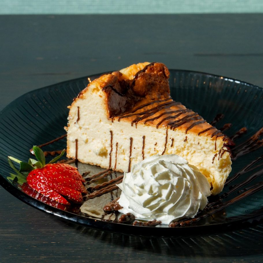 A slice of cake drizzled with chocolate, served with strawberries and whipped cream in London Restaurant